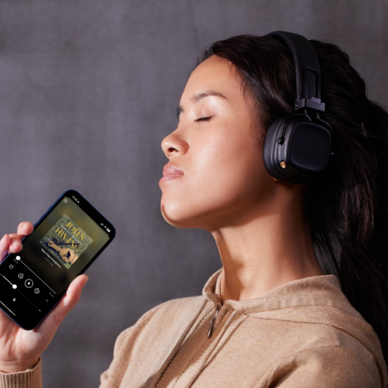 Kvinde der lytter til en lydbog med lukkede øjne, mens hun holder sin telefon i hånden