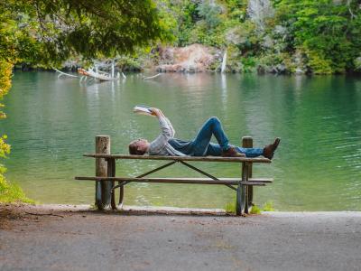 mand der ligger på bord og læser foran en skovsø